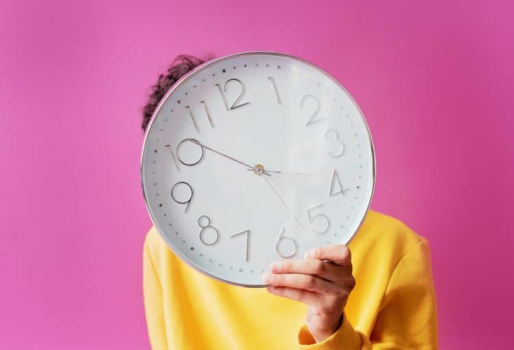 A person holding a clock in front of their face