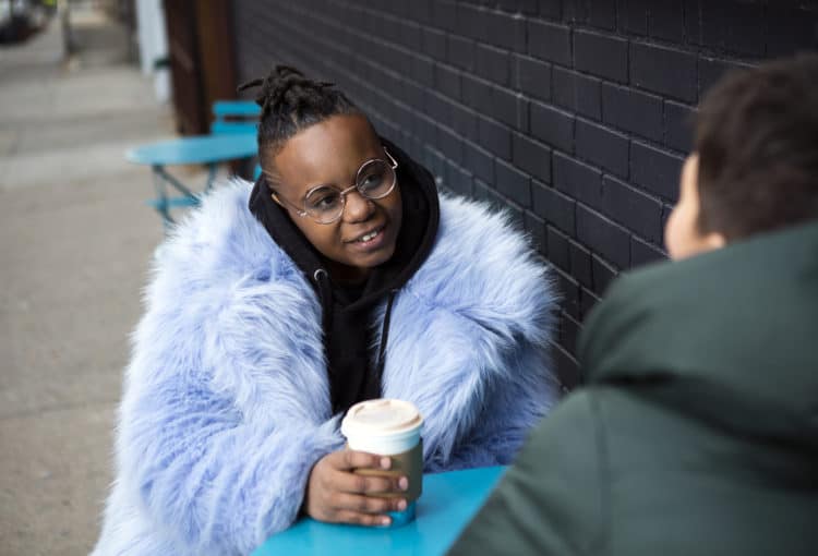 A-transmasculine-person-with-a-furry-blue-coat-drinking-coffee-with-a-friend-scaled