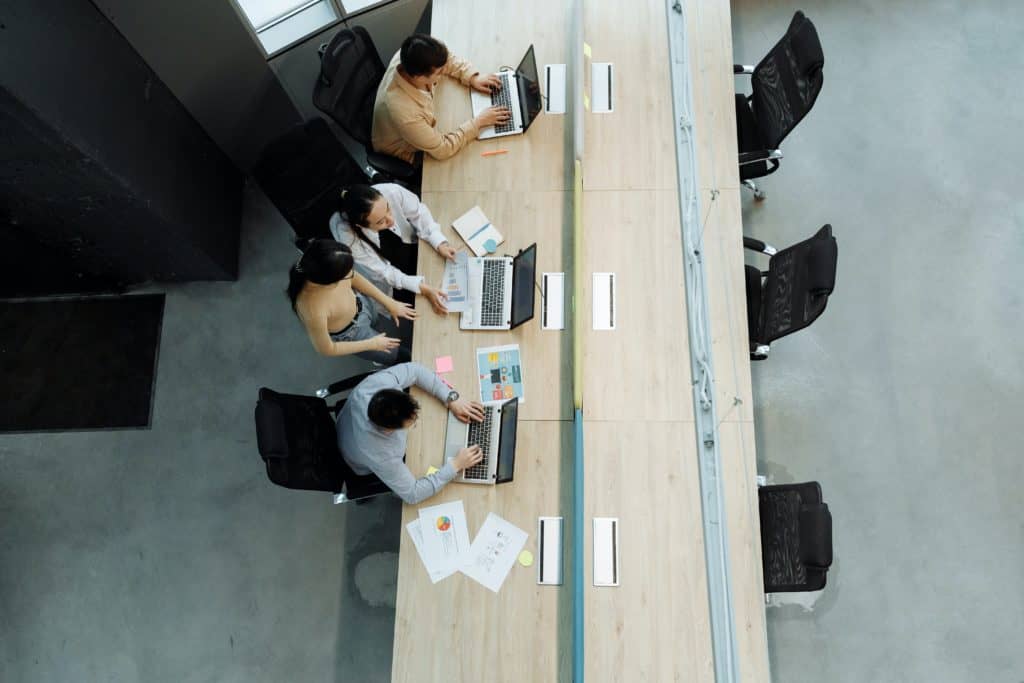 A group of people working at a table, possibly using Microsoft Teams.