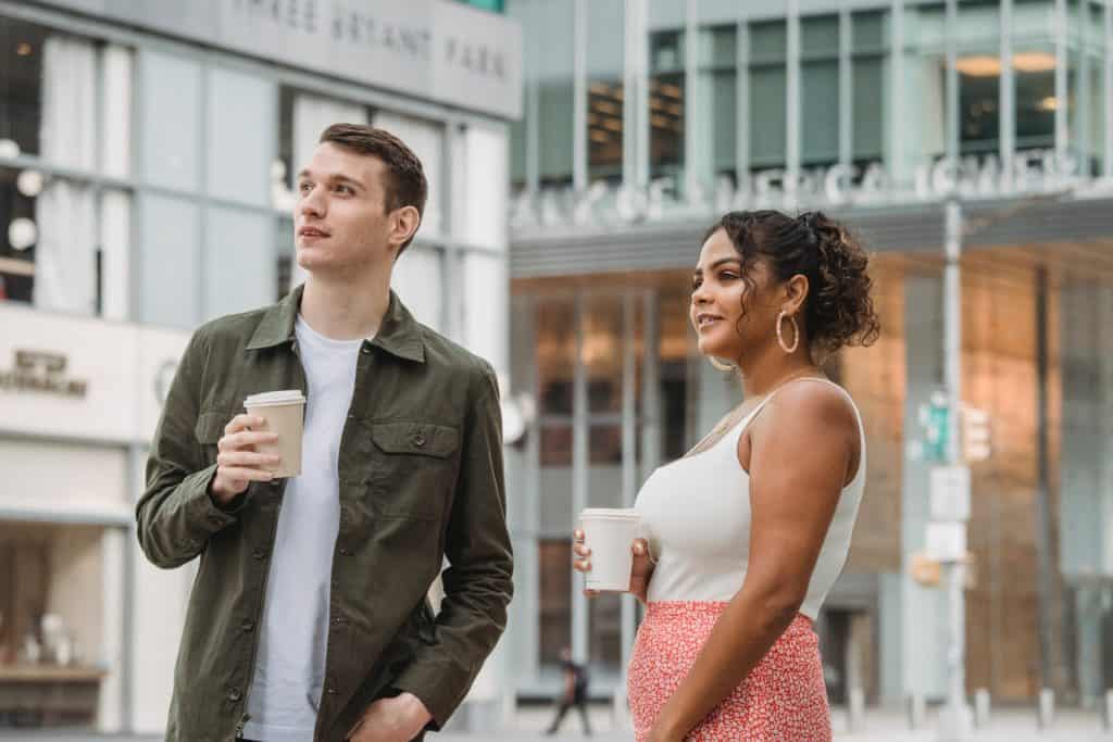 two people holding coffee cups and looking into the distance. Possibly listening with empathy.