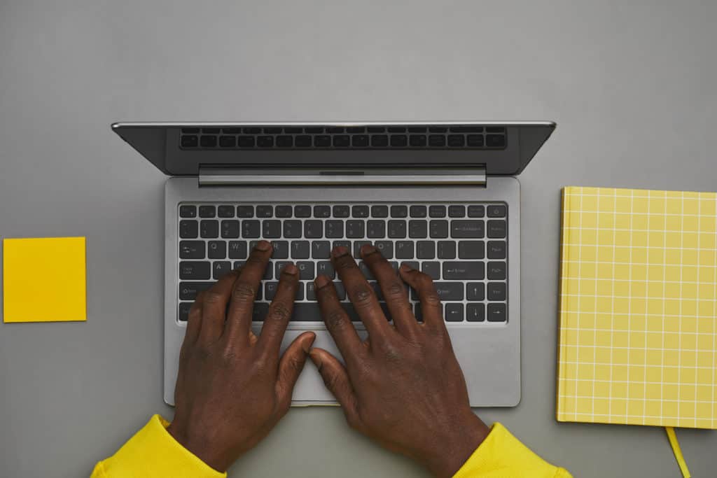 Graphic gray and yellow background of hands typing on laptop (possibly using Microsoft 365 / 2021) keyboard while working at desk, top down view, copy space
