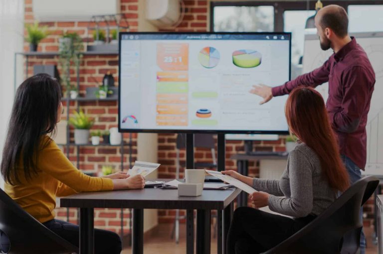 one person presenting a PowerPoint presentation. Two people watching the presenter and presentation.
