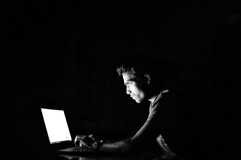 A man in a black room on a laptop