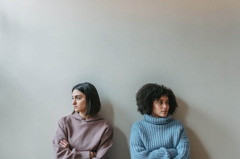 two people standing against a wall looking away from each other